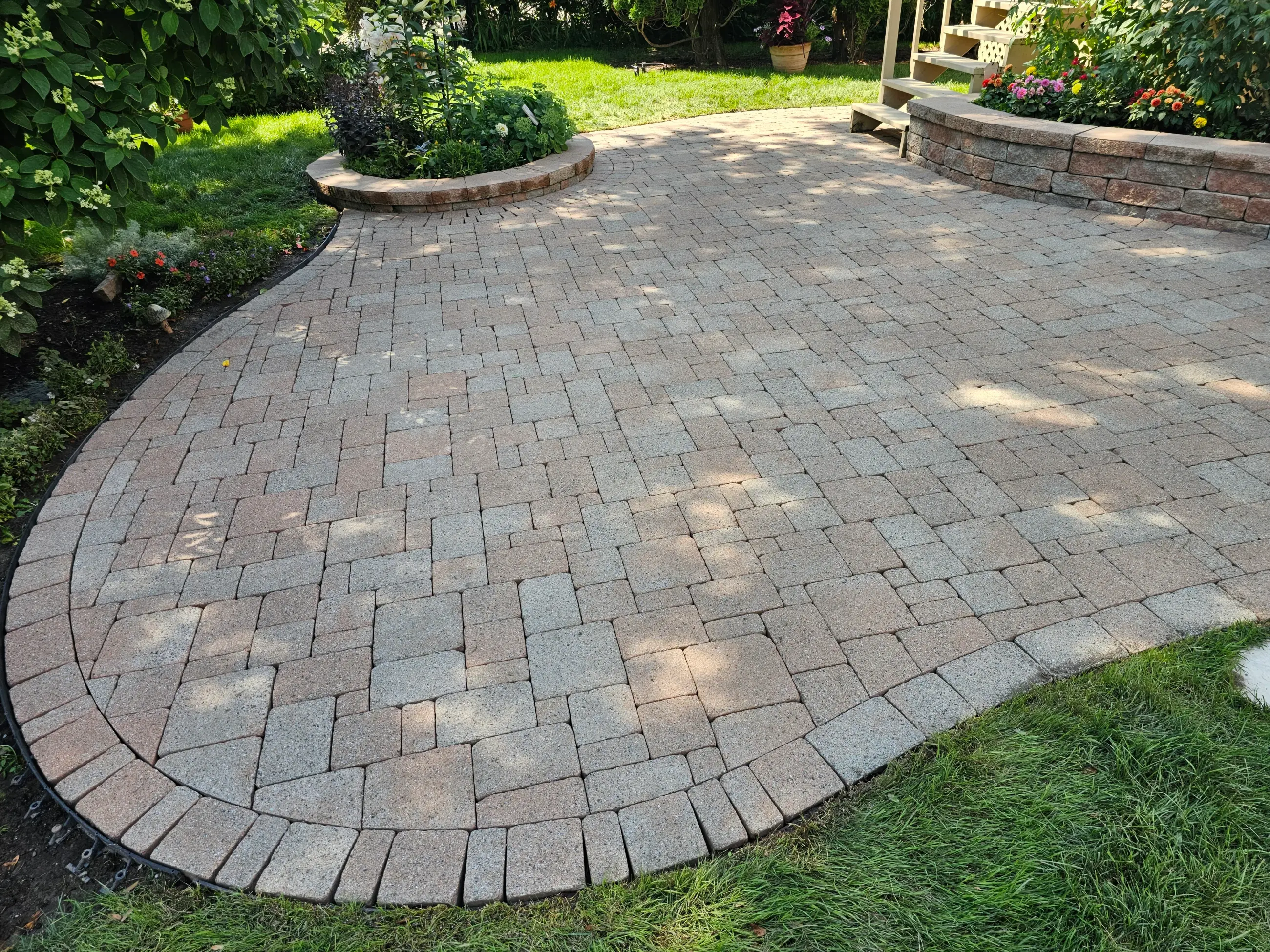 Restored multi-tone curved interlock patio framed by lush garden beds — a David's Lawns job