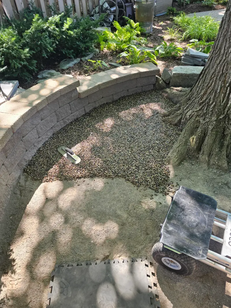 Fresh pea-gravel tree surround being installed with a cart in dappled shade
