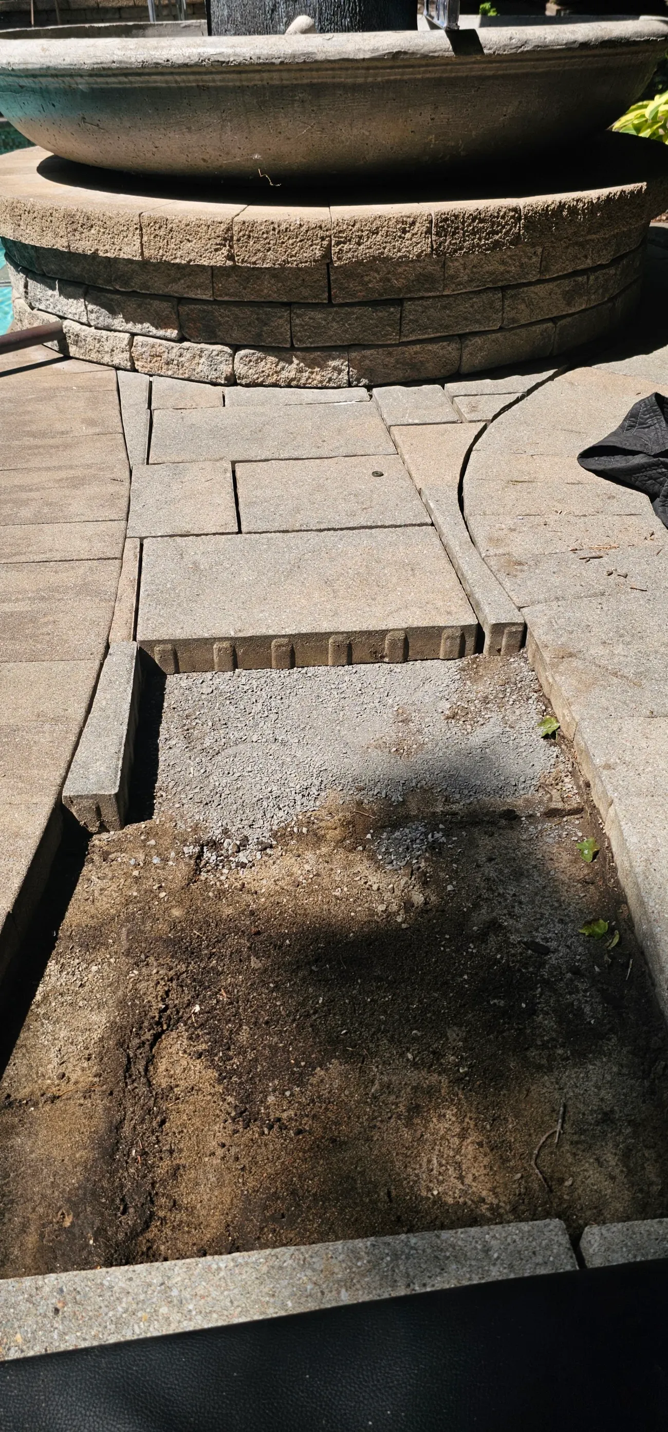 Pavers lifted beside a fountain ring exposing gravel bedding and edge restraint