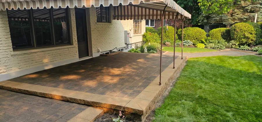 CAT5-sealed raised patio under a striped awning beside a thick green lawn in evening light