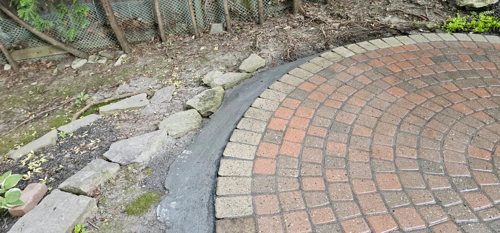 Freshly troweled concrete edge restraint locking the border pavers of a circular feature in place