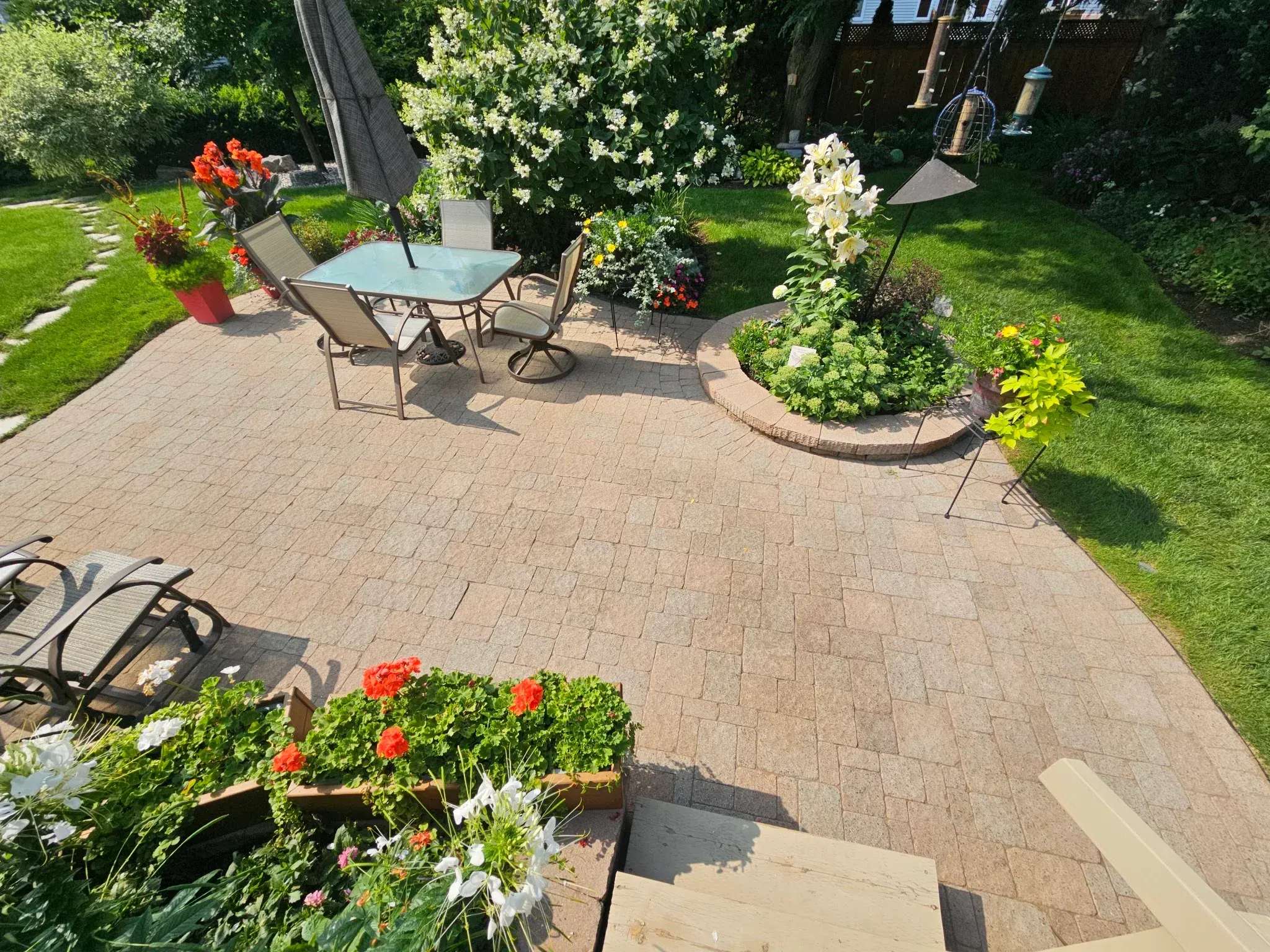 Restored backyard paver patio seen from the deck — crisp joints, circle garden bed, lawn on both sides