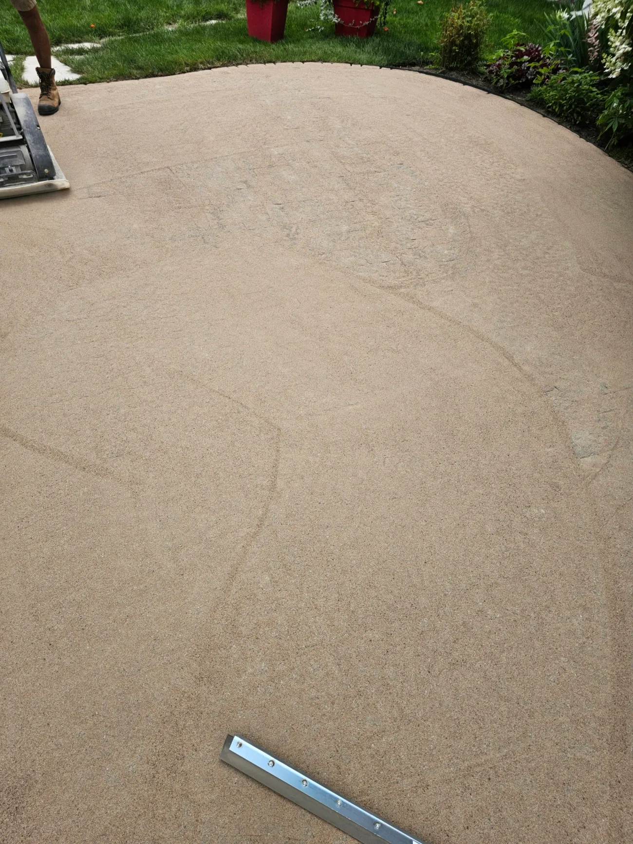 Patio flooded with polymeric sand mid-install, plate compactor and screed bar in frame