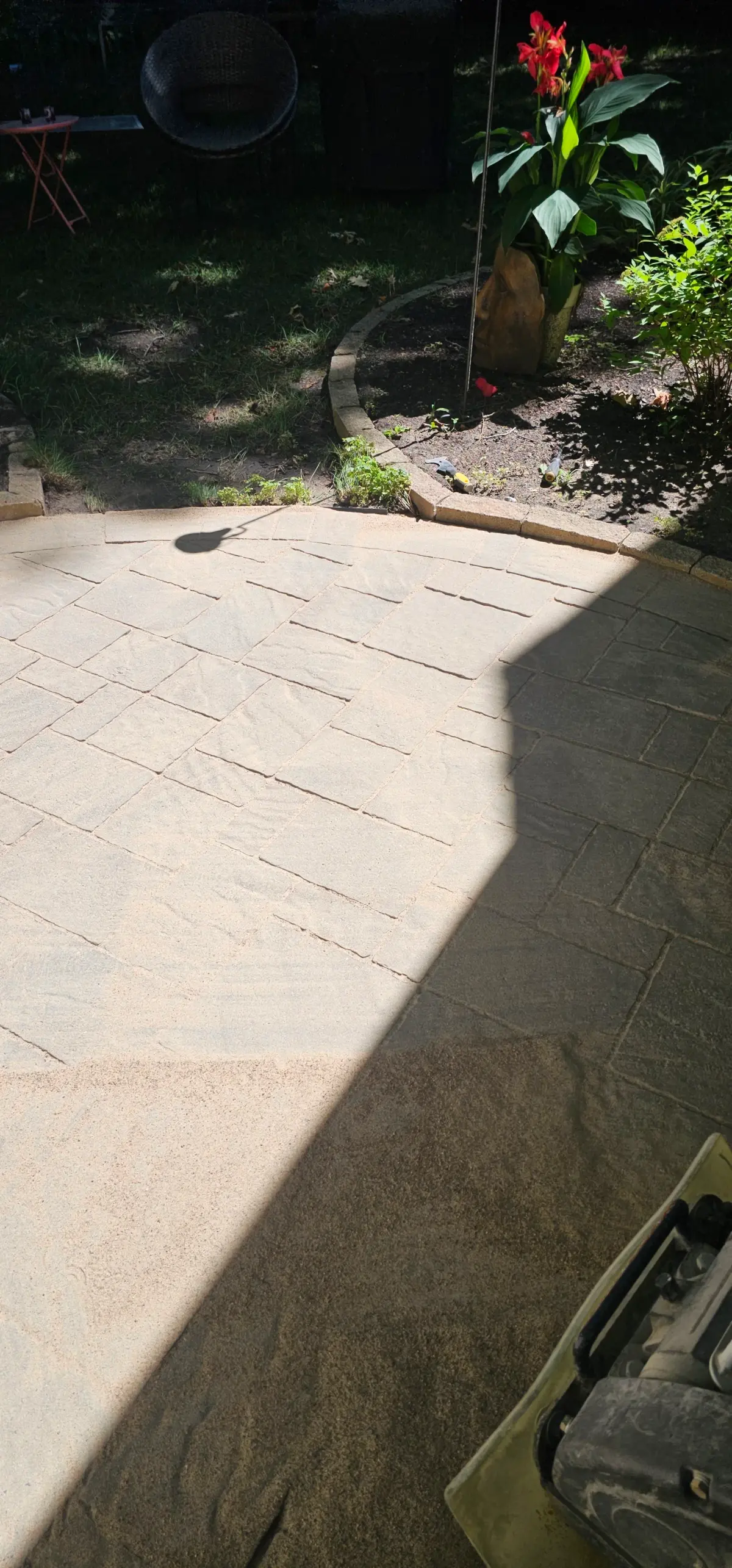 Thick blanket of polymeric sand spread across a paver patio with the plate compactor at the corner