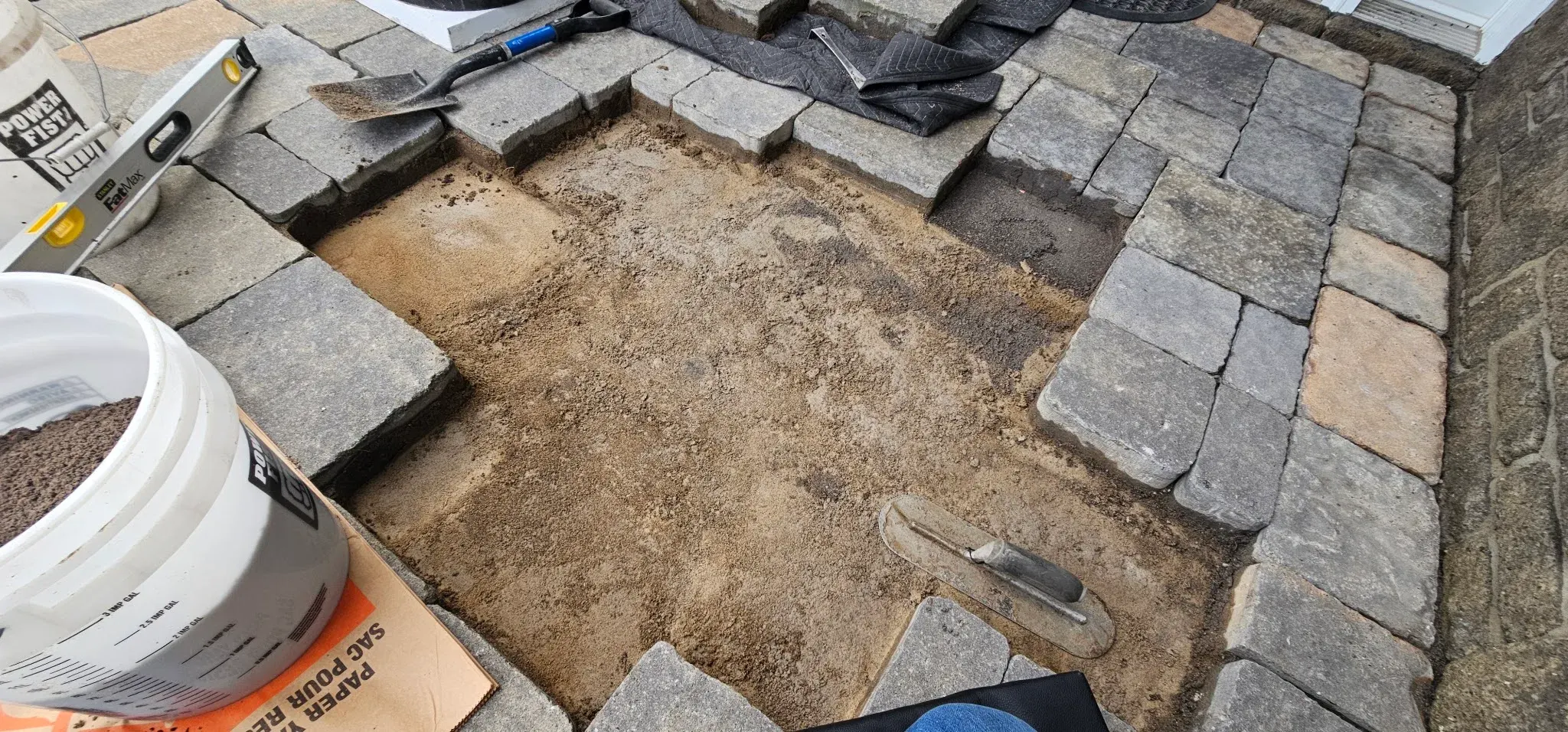 Pavers lifted aside with the bedding layer being screeded flat using a level and trowel, screenings bucket alongside