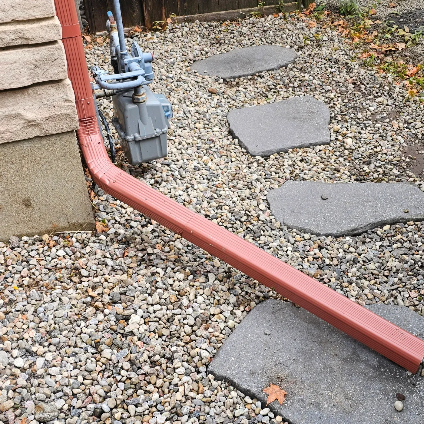 The same side strip after the clean, bright stone around the downspout and the stepping stones, no weeds